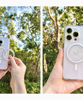 Person holding an iPhone with a slick clear magnetic base for PopSocket grips, compatible with MagSafe accessories, in a nature setting.