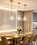 Super Sleek Brushed Gold Pendant Light For Kitchen Island Featuring Fully Adjustable Hanging Cord And Large Clear Glass Shade above modern dining table.