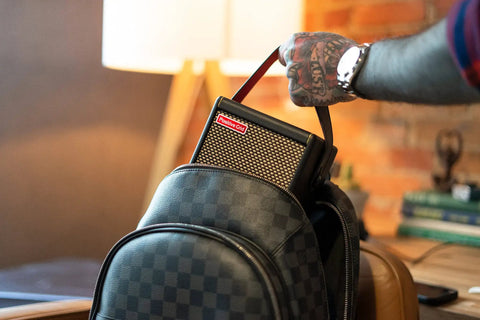 Person placing Spark MINI 10W Portable Guitar Amp And Bluetooth Speaker into a backpack, showing portability and ease of use.