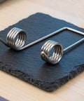 Heavy Duty Double Leg Torsion Springs For Trash Can Lid Repair Kit with 4 Coils Stainless Steel Garbage Bin Accessories Strong 130 Degree Angle Heavy Gauge Wire To Fix Stuck Lids Fast And Easy, shown on slate