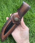 Hand holding Rugged Leather Knife Sheath For Fixed Blade Knives With Secure Buckle Scabbard Pouch on grass background