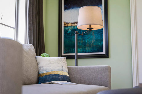 Riverside Copper Bronze Swing Arm Floor Lamp With Cozy Warm Glow Oatmeal Drum Shade beside a sofa in a living room corner.