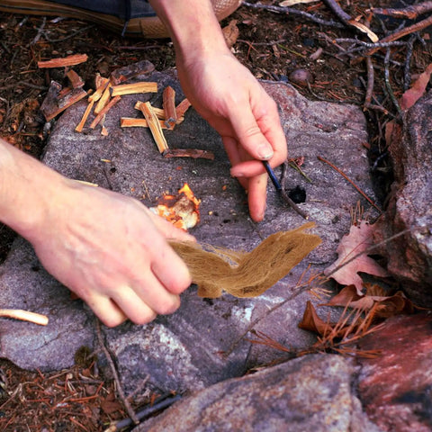 Hands using Jute Fire Starter Rope 4 Pack For Camping And Hiking Quick Ignition Twine Fire Starters on rocky ground outdoors