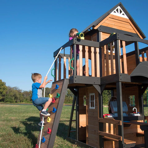 Children playing on Cedar Wood Swing Set With Wave Slide And Elevated Clubhouse Play Kitchen And Picnic Area Belt And Web Swings Rock Wall Balconies