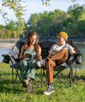 Two Person Padded Camping Chair For Outdoor Lounging with two people seated by a lake, showing cup holders, gray color