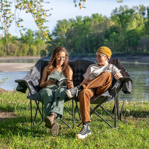 Two Person Padded Camping Chair For Outdoor Lounging with two people seated by a lake, showing cup holders, gray color