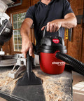 Man using 1.5 Gallon 2.0 Peak Wet Dry Vacuum for quick cleanups at home, garage, or vehicle with hose attachment on workbench.