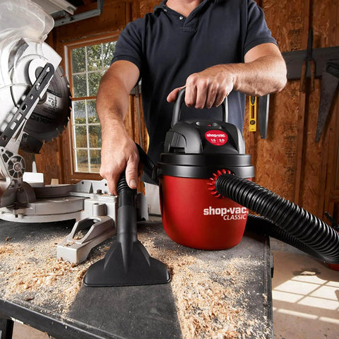 Man using 1.5 Gallon 2.0 Peak Wet Dry Vacuum for quick cleanups at home, garage, or vehicle with hose attachment on workbench.