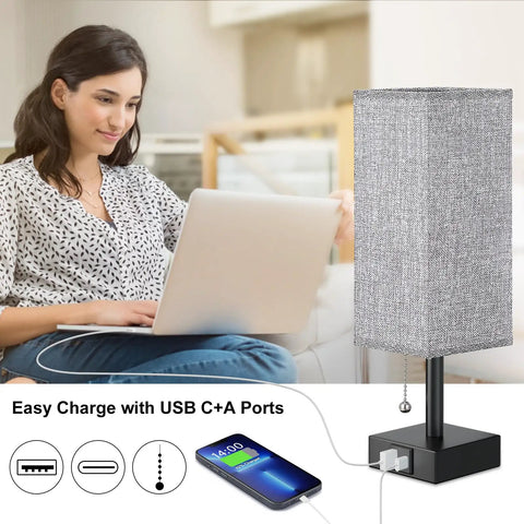 Woman using laptop beside gray bedside lamp with dual USB C and USB A ports for nightstand or small desk, chill light charges phone.