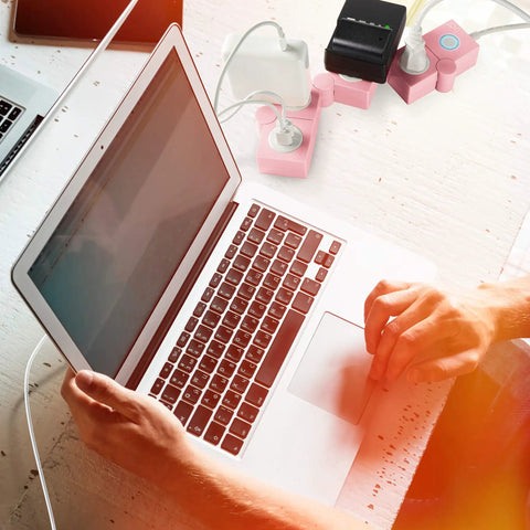 Person using a laptop with a pink power strip with surge protection, 3 AC outlets and 2 USB ports, flexible twist design on desk.