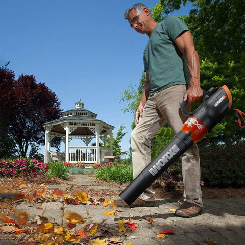 Man using 12 Amp Electric Leaf Blower With Turbine Tech for yard cleanup, clearing leaves on stone path, gazebo in background.