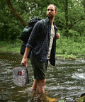Man crossing stream with 125 Piece Survival Kit For Outdoorsy Folks And Women, Ultimate Backcountry Emergency Gear in hand