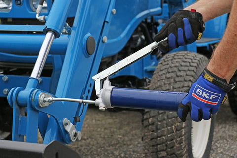Side view: Lincoln 1142 lever-action grease gun with 6-inch extension on blue hydraulic frame; cast-iron pump head