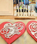 Two red heart-shaped wooden Valentine plaques with white laser-cut roses; drill-bit organizer in the background.