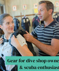 A person assisting another to wear scuba gear in a dive shop.