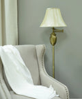 Wellington Steel Swing Arm Floor Lamp In Antique Brass, next to beige armchair, with round faux silk shade, in living room.