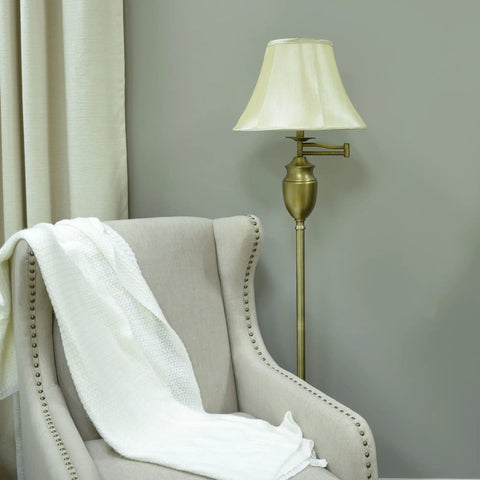 Wellington Steel Swing Arm Floor Lamp In Antique Brass, next to beige armchair, with round faux silk shade, in living room.