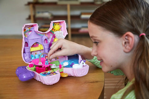 Child playing with Unicorn Party Playset With 25 Surprises, pink unicorn toy with purple hair, open to reveal castle adventure scene