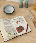 Premium Hardcover Blank Recipe Book For Your Own Creations A DIY Family Cookbook open on a kitchen table with utensils.