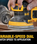 Hand adjusting speed dial on 20V Max Brushless Random Orbital Sander Kit With Variable Speed 8,000 To 12,000 OPM on wood surface.