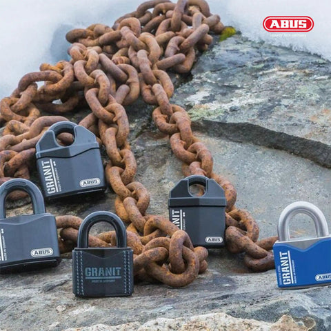 Image of several Granit 37/80 Beefy Heavy Duty Padlocks with hidden closed shackles resting on a rugged chain outdoors.
