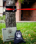 Slackline Kit With Overhead Training Line, Arm Trainer, Tree Protectors, and Carry Bag on grass by tree