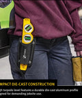 Person holding Die Cast Three Vial Torpedo Level With 1 Percent And 2 Percent Slope Rings in a work pouch, jobsite in background.