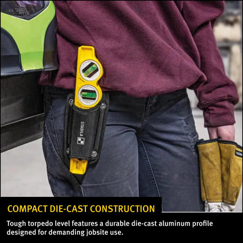 Person holding Die Cast Three Vial Torpedo Level With 1 Percent And 2 Percent Slope Rings in a work pouch, jobsite in background.
