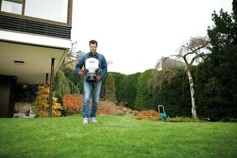 Person using 20 Pound Capacity Portable Chest Mount Spreader With Cross Shoulder Strap For Lawn Care And Garden Pros Easy Fill And Clean Hopper White 421S Granular Spreader With Fingertip Levers For Precise Control on lawn.