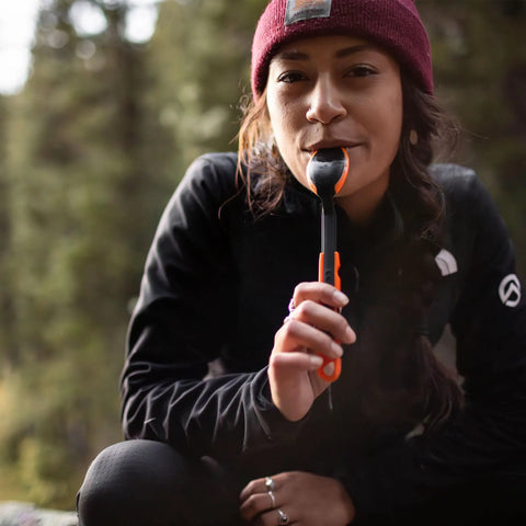Person outdoors holding TrailSpoon Extendable Backpacking Spoon With Silicone Edge For Pots Reach Inside Cookware during camping trip.