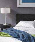 Stowe Table Lamp in Brushed Steel Finish With White Textured Drum Shade on nightstand in modern bedroom setting.