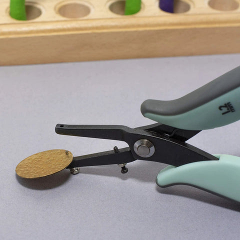 Metal Hole Punch Pliers With Gauge Guard for soft metals, showing 1.25mm hole punch on a brass sheet for jewelry making.