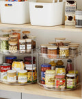 Front view of two-tier clear acrylic Lazy Susan turntables with chrome frame on pantry shelf, holding jars.