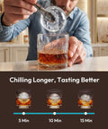Man placing ice sphere into whiskey glass using Crystal Clear Ice Ball Maker For Countertop 2.4 Inch Spheres 2 Piece Set