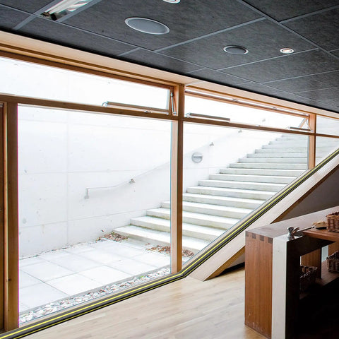Indoor space with large glass windows and wooden interior, showing outdoor steps and natural light.
