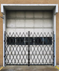 Tough As Nails Double Folding Security Gate Steel Accordion Expanding Barrier with Smooth Rolling Casters and Secure Lock in front of garage door.