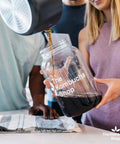 Individuals pouring tea into a glass jar for Organic 1 Gallon Kombucha Starter Kit With SCOBY Fermentation Jar Tea And Sugar Bottling Essentials And Clear At Home Brewing Instructions For Beginners To Kickstart Your Brew Like A Pro.