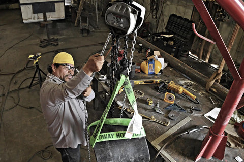 Worker using Half-Ton Hand Chain Hoist with 10 ft lift in industrial setting, 360 degree rotating alloy steel hooks in view.