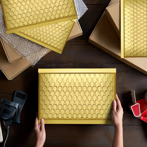 Hands holding a gold bubble mailer from a 6x10 pack, featuring metallic surface and bubble padding for jewelry shipping.