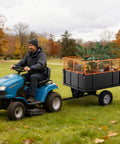 Man towing Beefy Heavy Duty Steel Dump Cart With 17 Cu Ft Bed 750 Lb Capacity Removable Sides across lawn with tractor