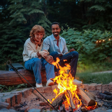 Two people sitting by a bonfire using Beefy 40 Inch Heavy Duty Fire Poker With Twisted Rope Grip Solid 12mm Steel Wrought Iron Fireplace Tool.