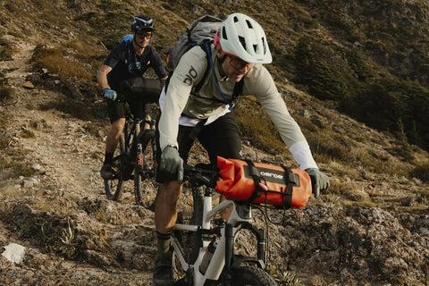 Cyclists riding mountain trails with Spider Handlebar Cradle With 8L Heavy Duty Dry Bag For MTB Gravel And EMTB Bikes Quick Release Mount