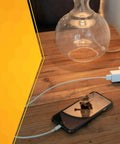 Slimline Flat Plug Extension Cord 6 Foot 16 Gauge 3 Conductor 3 Outlet Indoor White powering phone and lamp on table.