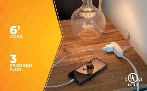 Slimline Flat Plug Extension Cord 6 Foot 16 Gauge 3 Conductor 3 Outlet Indoor White powering phone and lamp on table.