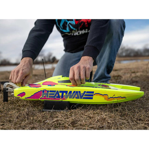 Person placing the Blackjack 24 Inch V2 Catamaran Brushless RC Boat with Heat Wave Visual on grass, showing bold two-tone trim.