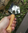 Hand holding Built To Last Stainless Steel Garden Shovel With Ergonomic Wooden Handle for digging in soil near stone