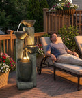 Outdoor 40 Inch Water Fountain with LED lights, 4 tier crocks waterfall decor on patio; weather-resistant polyresin design with man relaxing nearby.