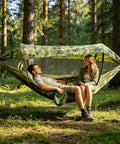 Two people relaxing in a forest with a Camping Hammock Tent With Net And Portable Sleeping Cot For Backpacking And Hiking Travel 3 In 1 All In One Outdoor Gear With Rain Fly Heavy Duty 440 Lbs Capacity.