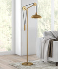 Solid Wheel Pulley Floor Lamp With Brass Dome Shade And Industrial Steel Base next to a sofa, in a sunlit living room