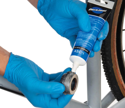 Park Tool ASC-1 anti-seize compound applied to bicycle bearing area; blue-gloved hands